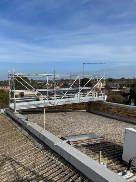 Scaffolding on a flat roof, overlooking a town under a blue sky.