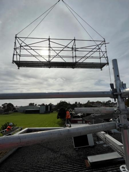 Scaffolding being lifted by a crane over a roof for construction on a cloudy day.