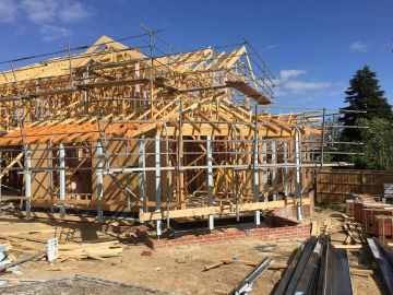 Wooden house under construction with scaffolding, sunny day.