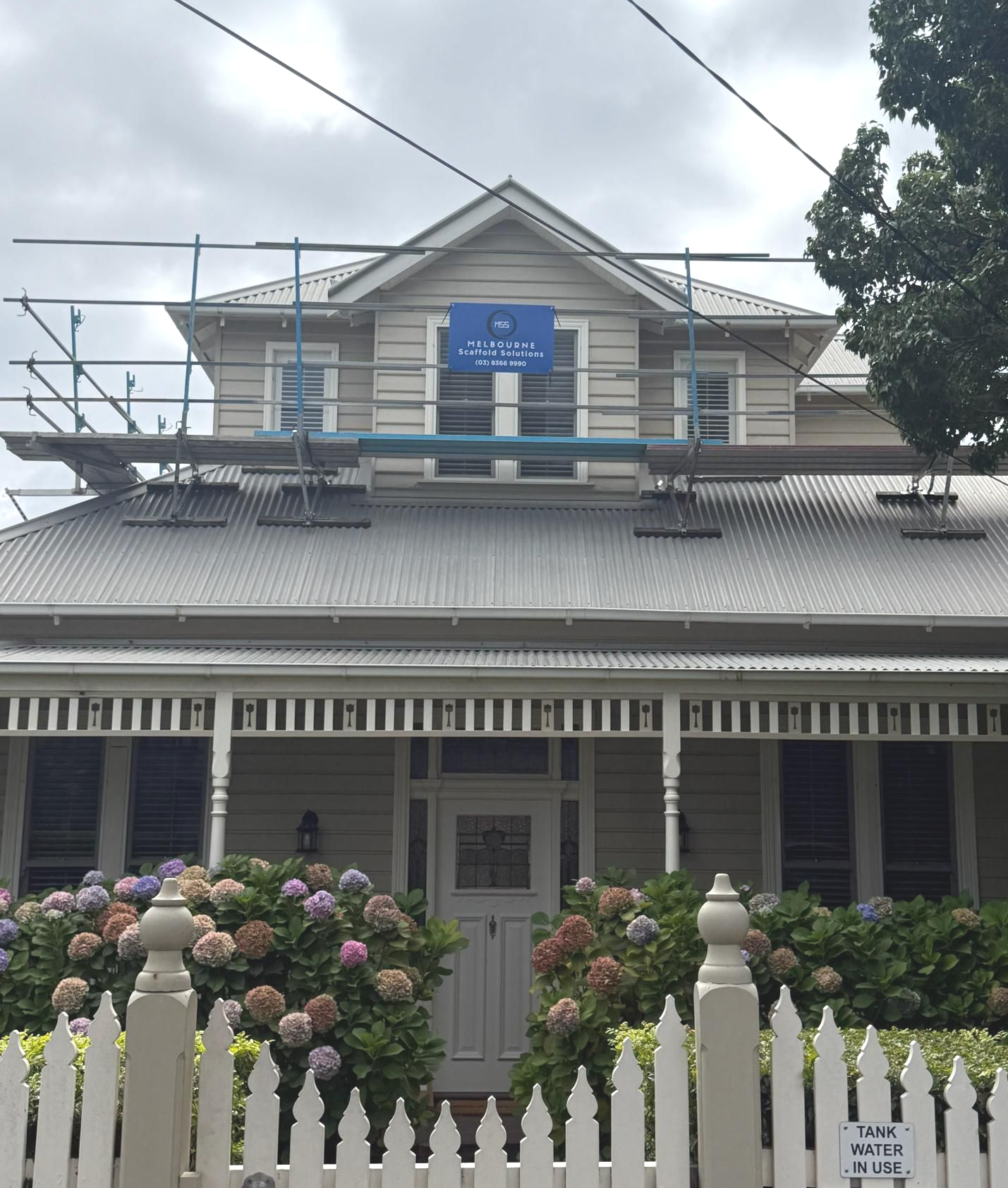 Scaffolding around a building's roof for construction work. Red safety netting and grey building.