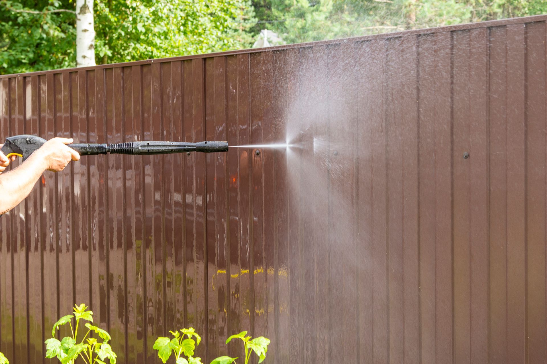 A man is using a high-pressure washer to clean a wooden fence — Cave Spring, GA — Straight Shooter Pressure Washing