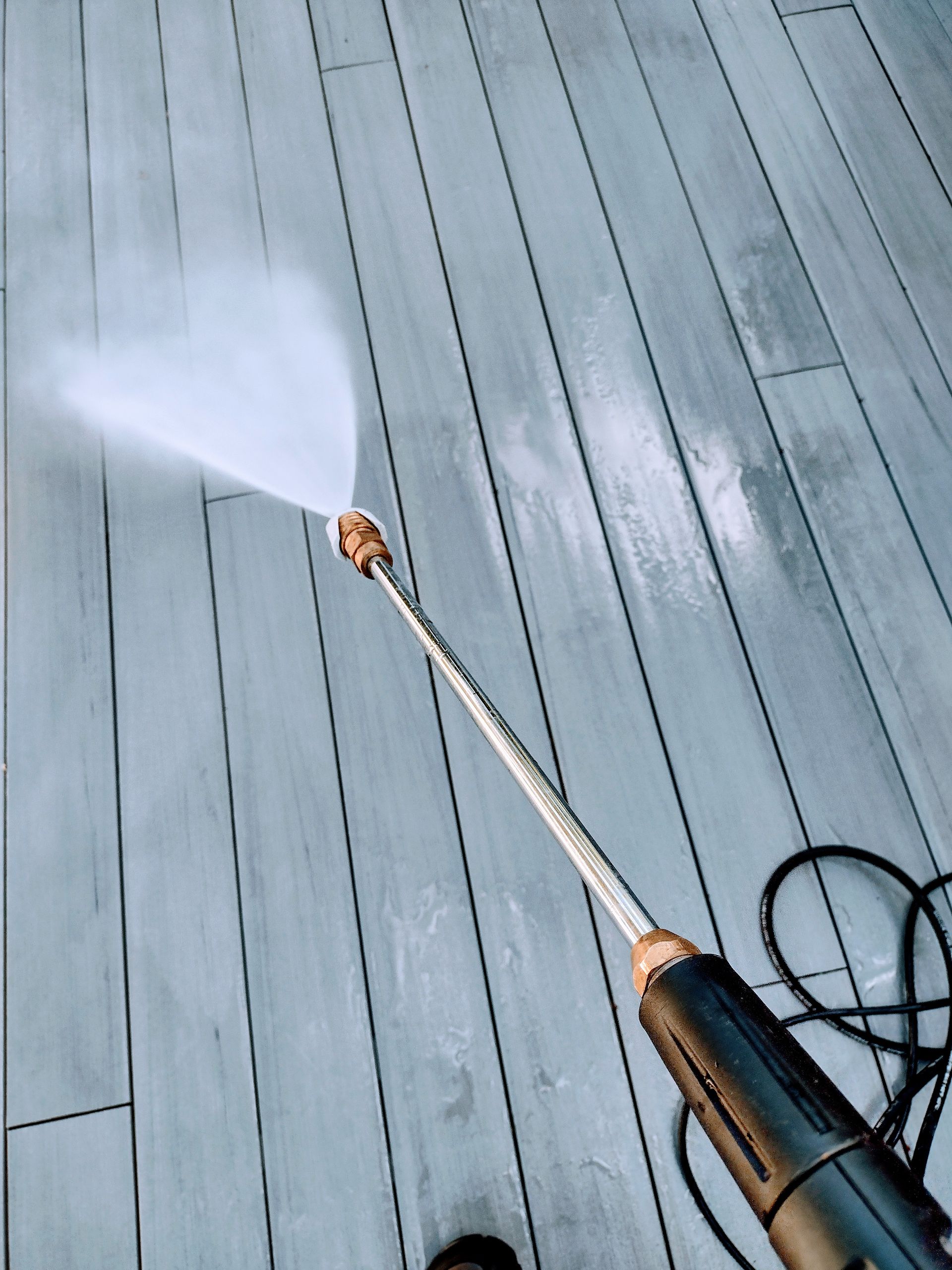 A person is using a high-pressure washer on a wooden deck — Cave Spring, GA — Straight Shooter Pressure Washing