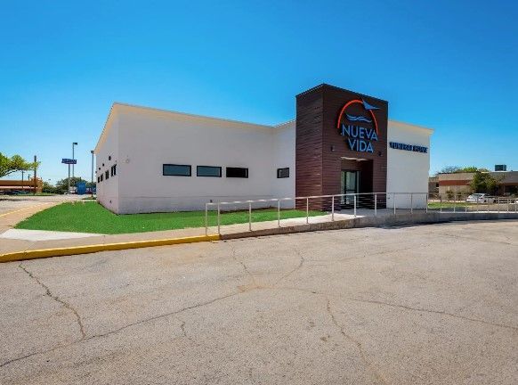 Modern white building with a dark brick entrance sign under a bright blue sky