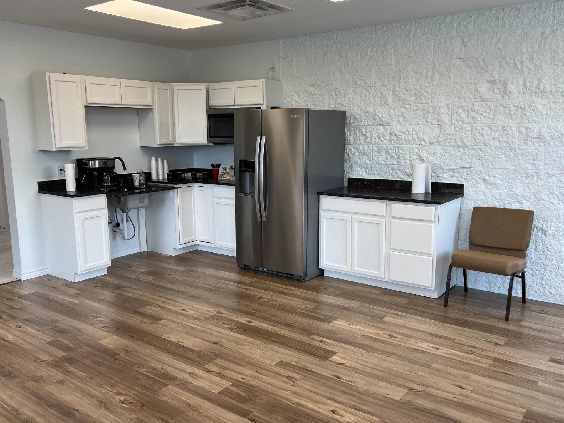 Cocina luminosa con armarios blancos, nevera de acero inoxidable, encimeras negras y suelo de madera.