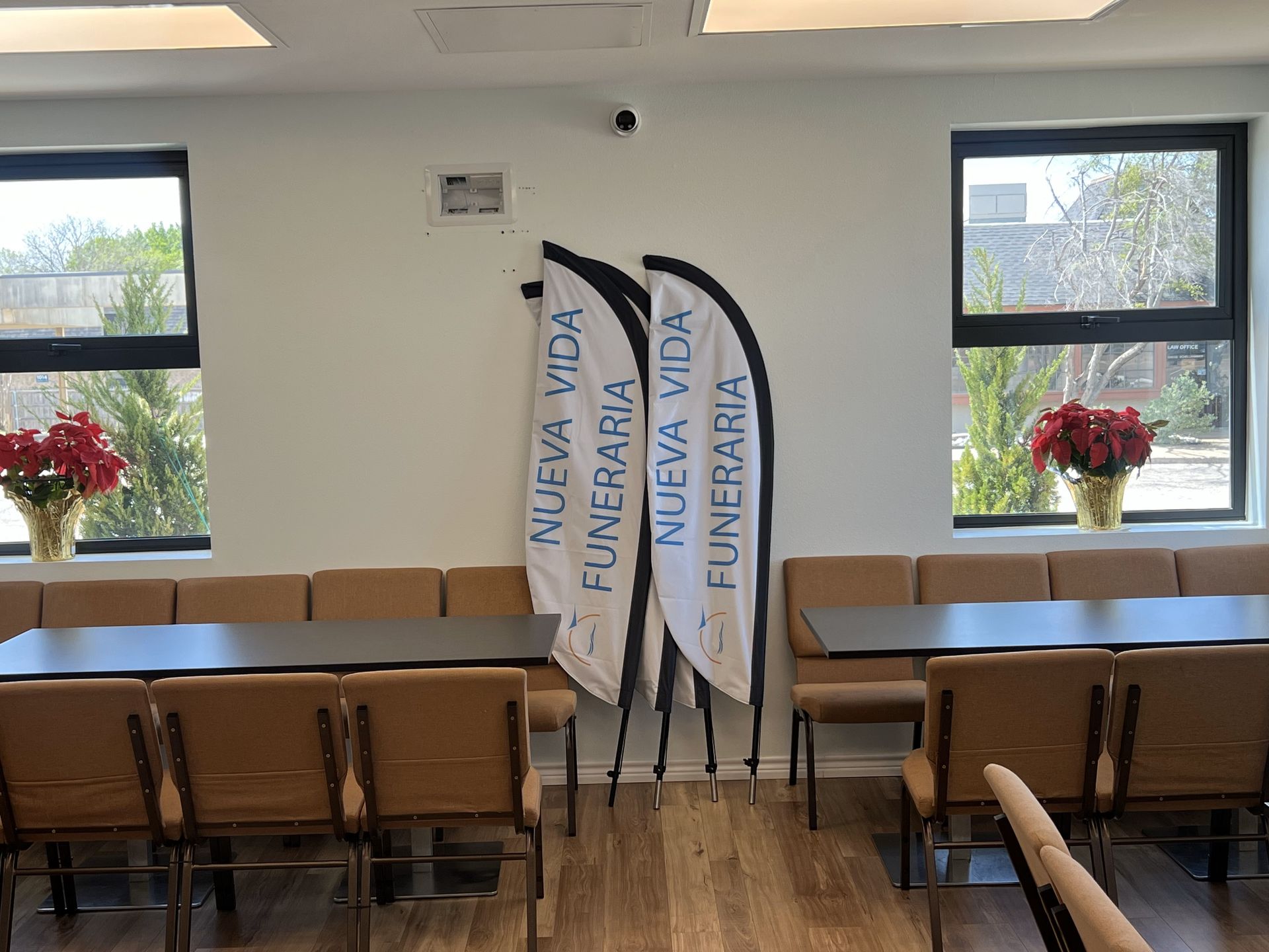 Indoor meeting room with wooden chairs, large windows, flower vases, and three branded vertical flags.