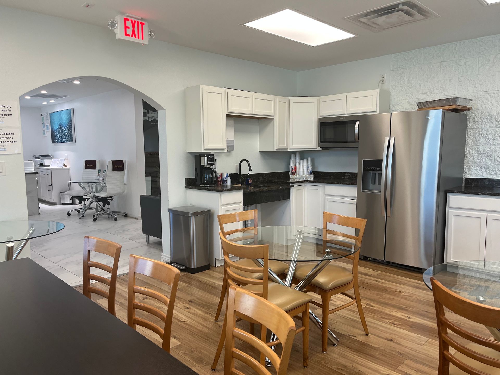 Kitchen and dining area with glass table, wooden chairs, stainless steel appliances, and an arched doorway to a workspace
