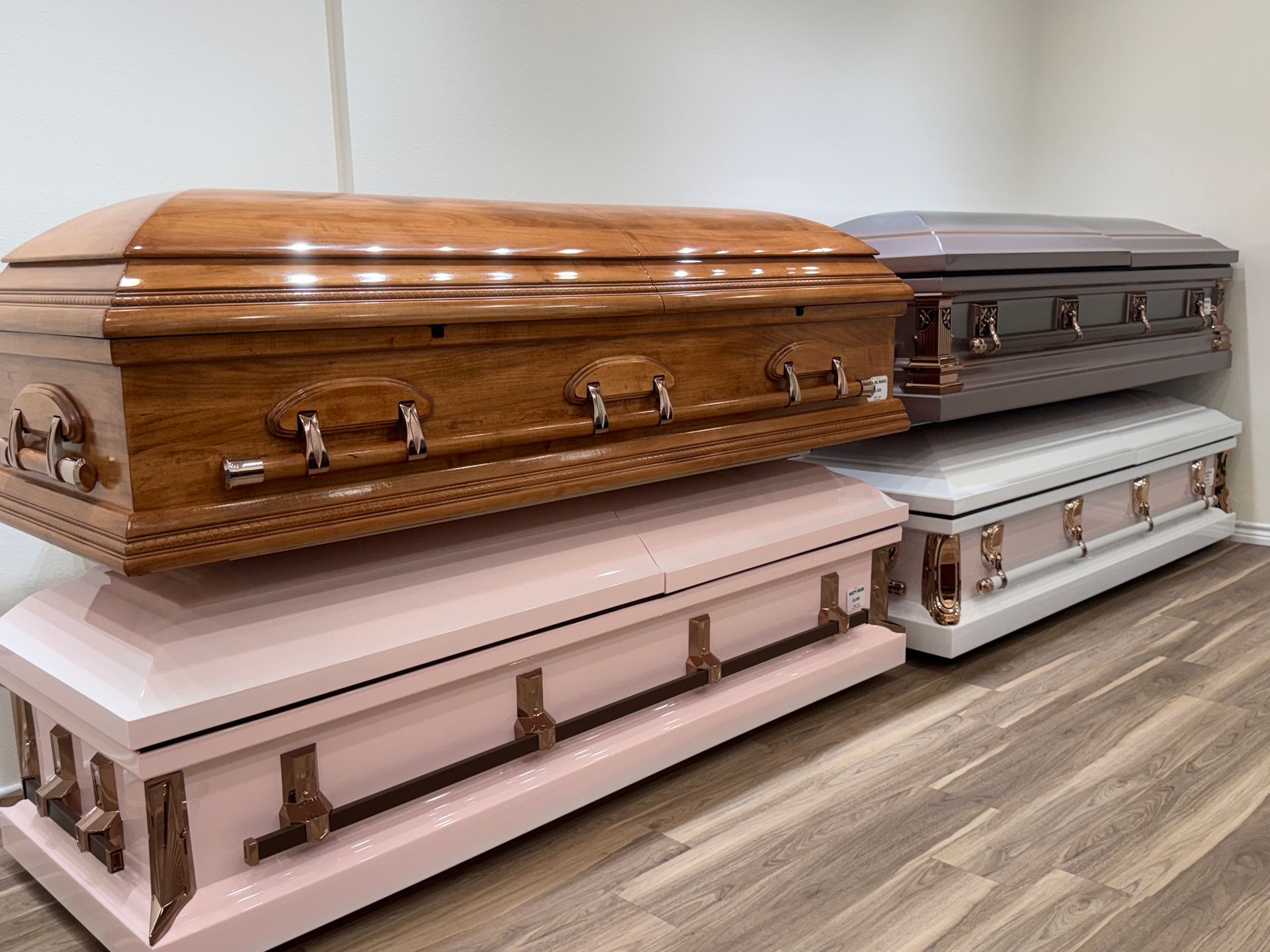 Row of four ornate coffins in wood, pink, gray, and white, displayed indoors on a floor