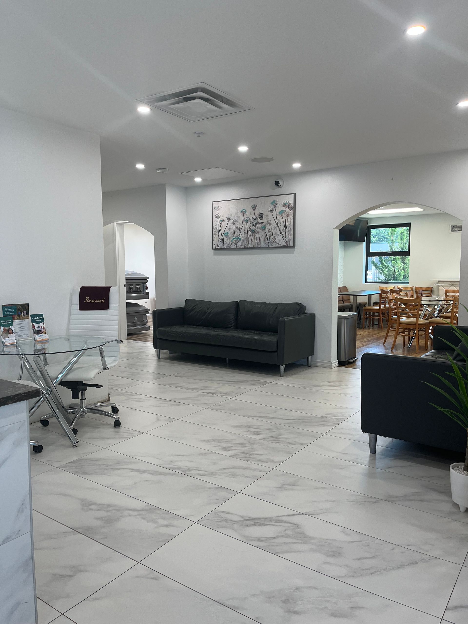 Bright white living room with black sofas, glass coffee table, and an arched opening to a dining area
