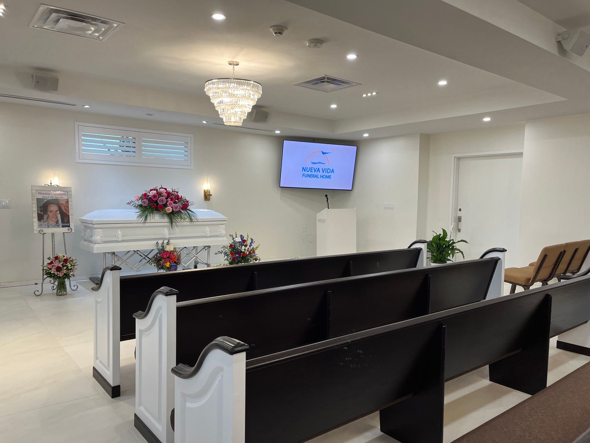 Modern chapel interior with white pews, altar flowers, chandelier, and wall-mounted screen