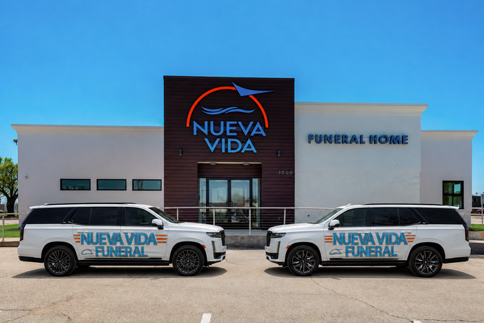 Two white funeral service SUVs parked in front of Nueva Vida Funeral Home under a clear blue sky