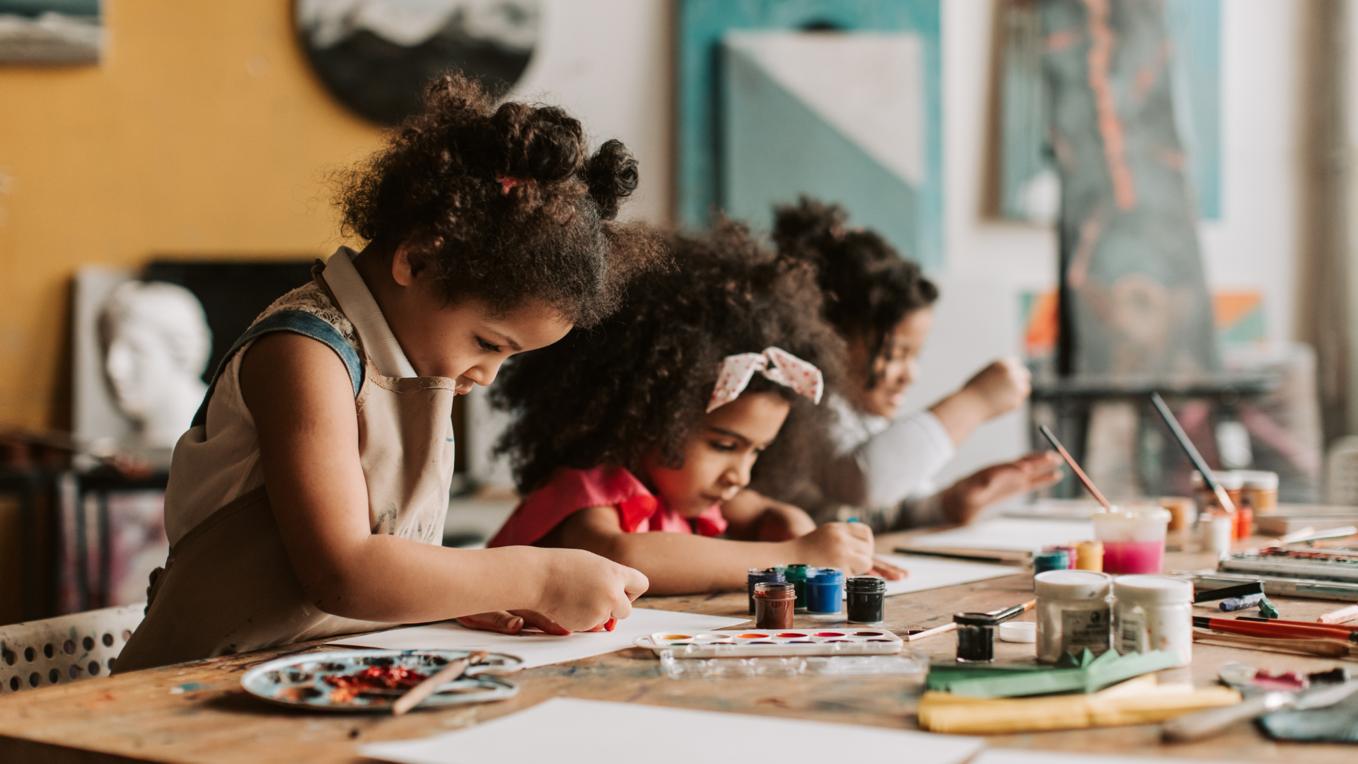 Children painting at a table with art supplies in a classroom.