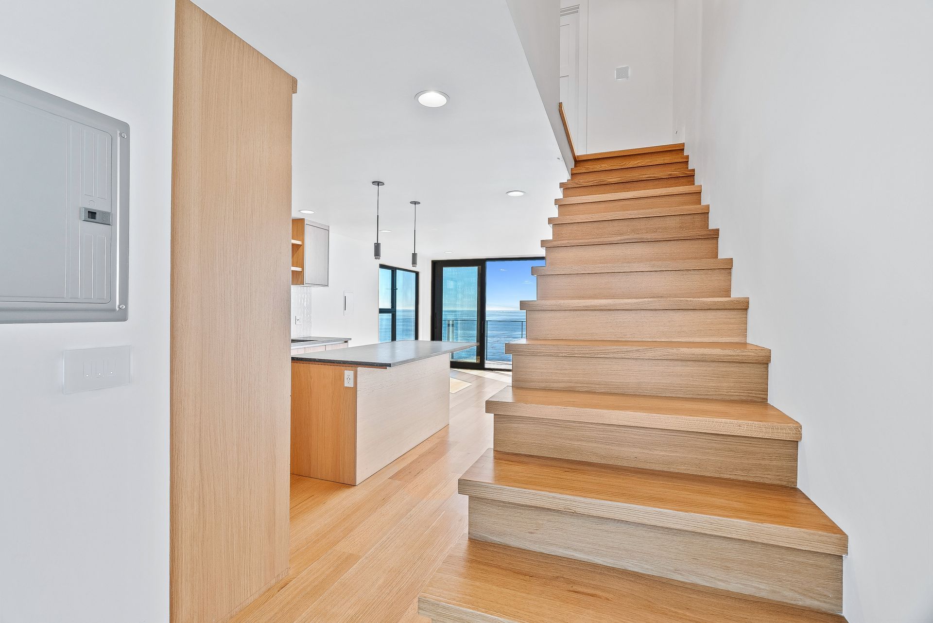 Bright modern interior with a wooden staircase leading up beside a kitchen and glass doors.