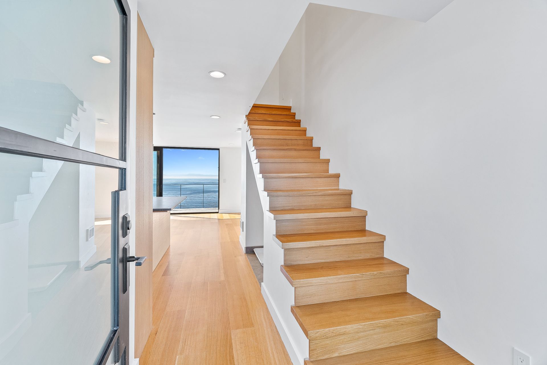Bright hallway with wooden staircase leading to ocean view through open doorway