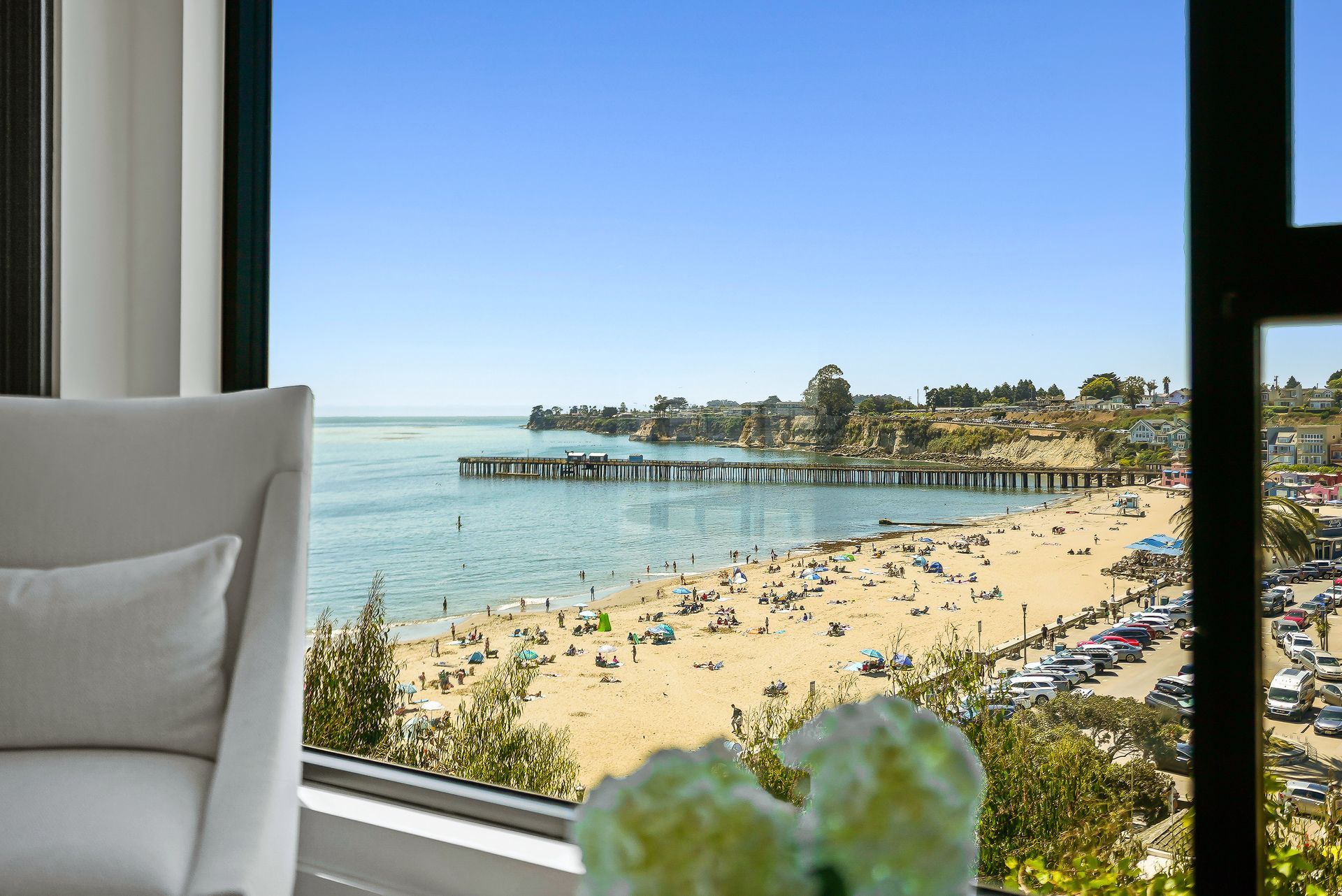 Beach view through a window with a pier, blue water, and people on the shore