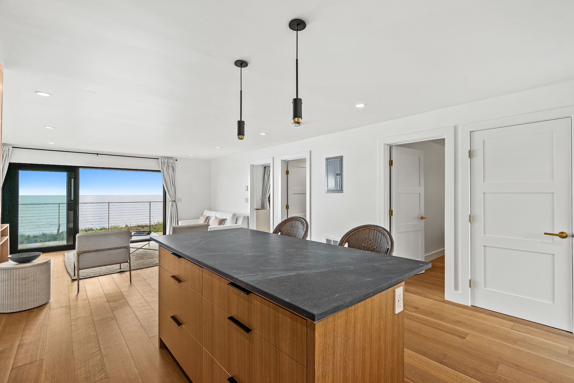 Modern kitchen and living space with island, hardwood floors, pendant lights, and sliding doors to a patio.