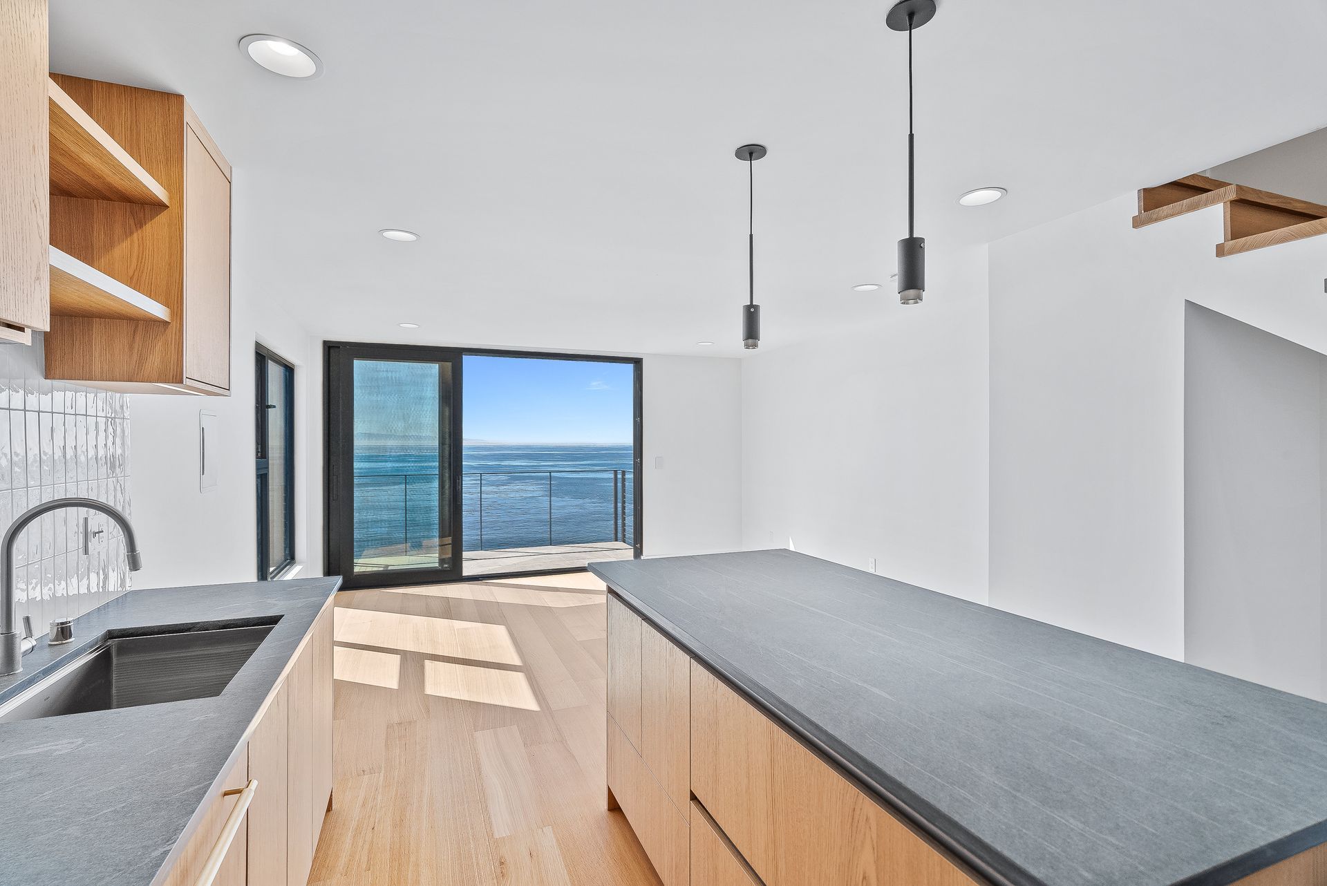 Modern kitchen with light wood island, black countertops, and open doors to a bright mountain view