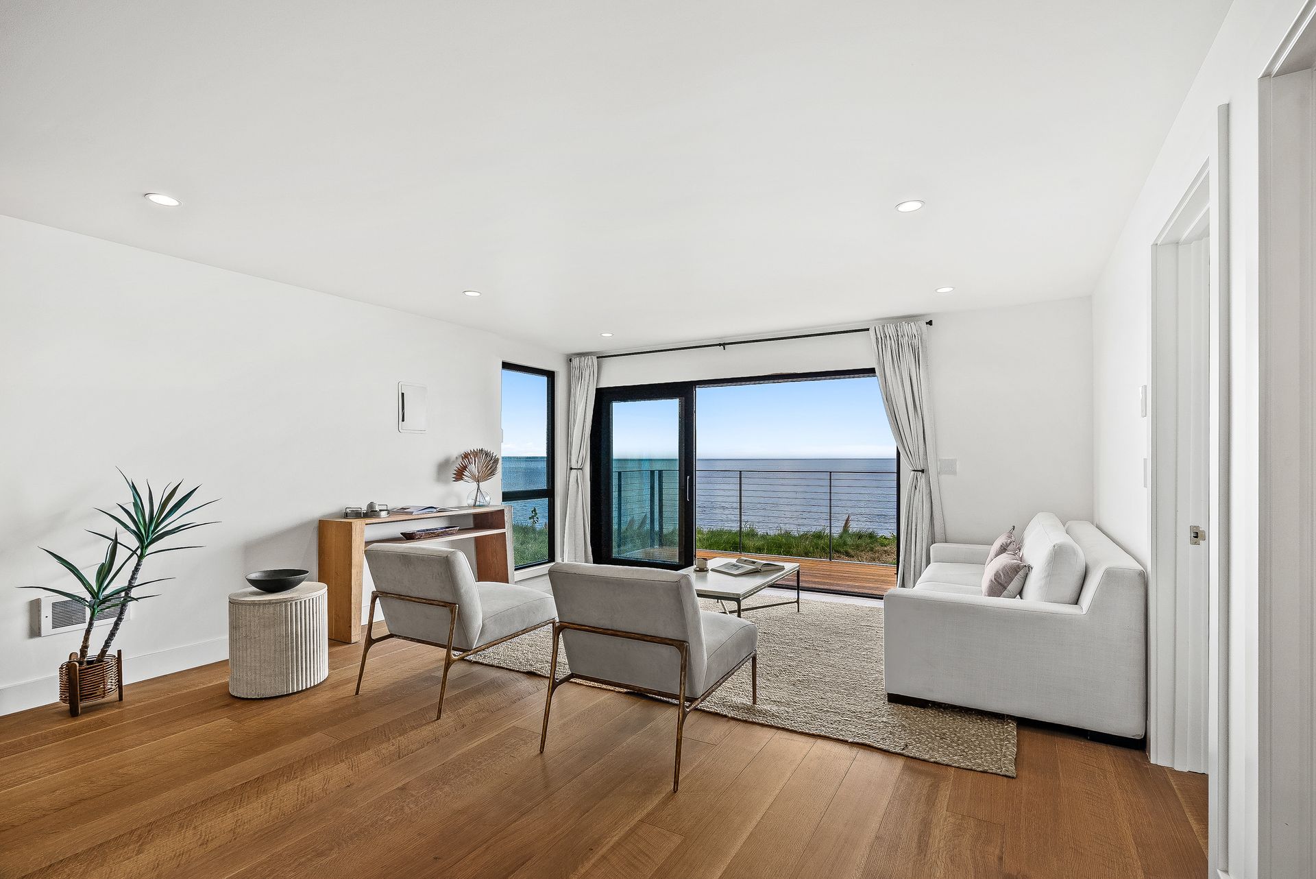 Bright living room with wood floors, gray seating, and open doors overlooking a balcony and ocean view