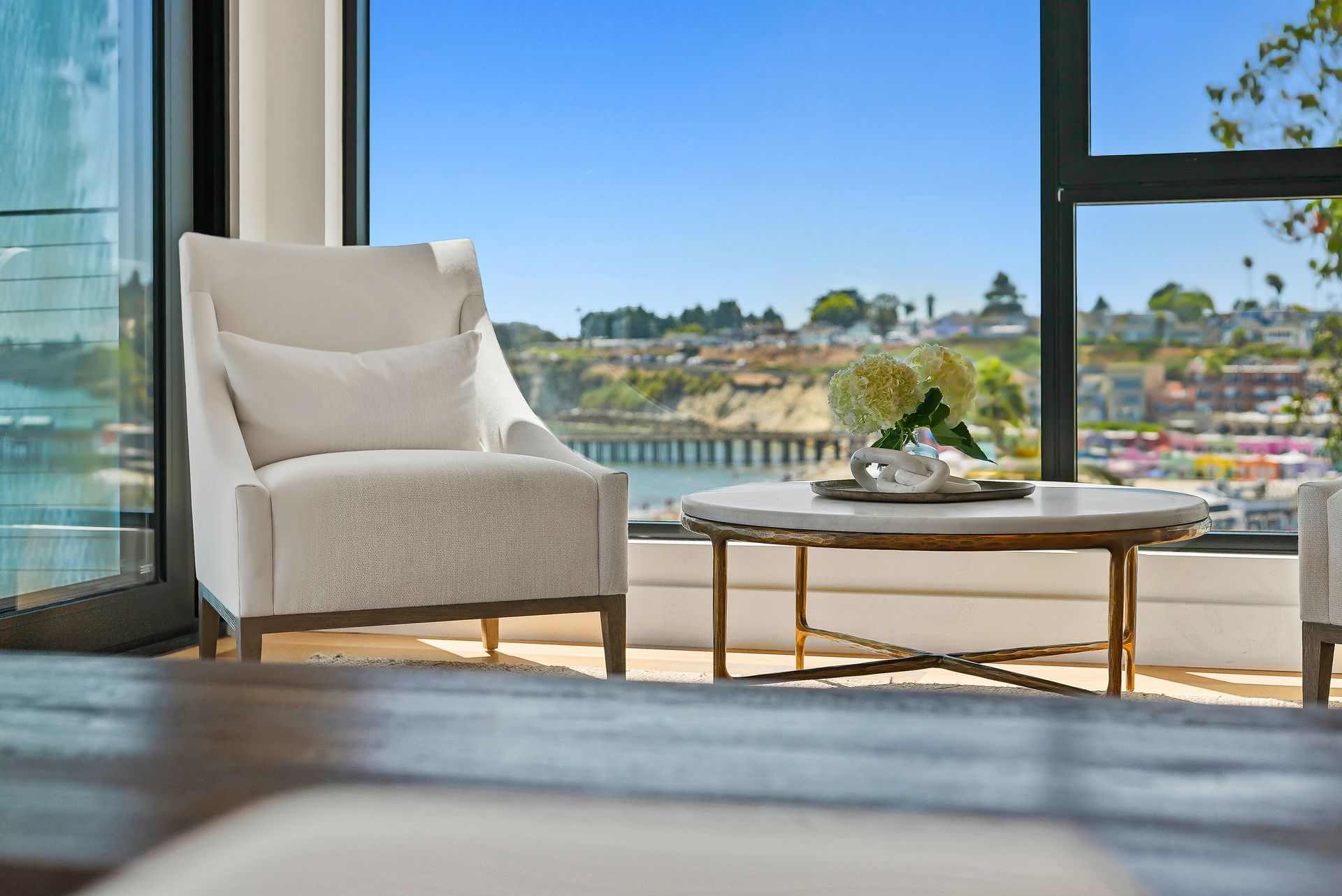 Modern living room with beige armchair and coffee table overlooking a waterfront view through large windows