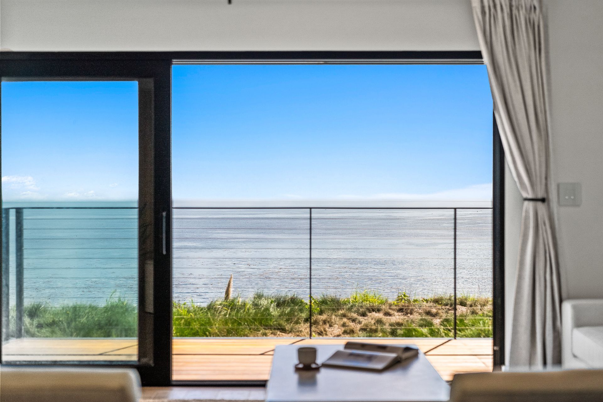 Modern living room with open sliding doors to a bright ocean view and balcony.
