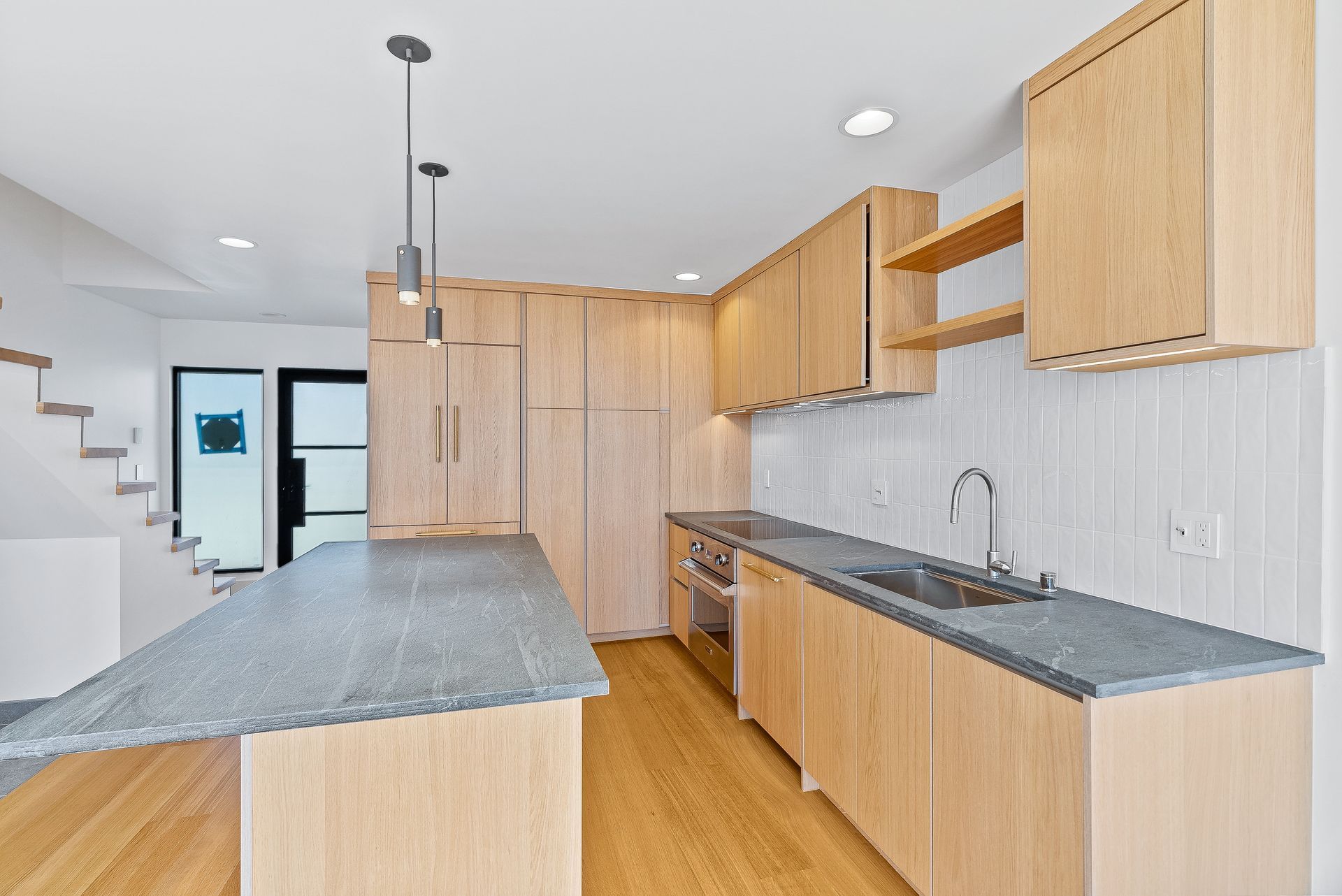 Modern kitchen with light wood cabinets, gray countertops, and a central island in a bright open room