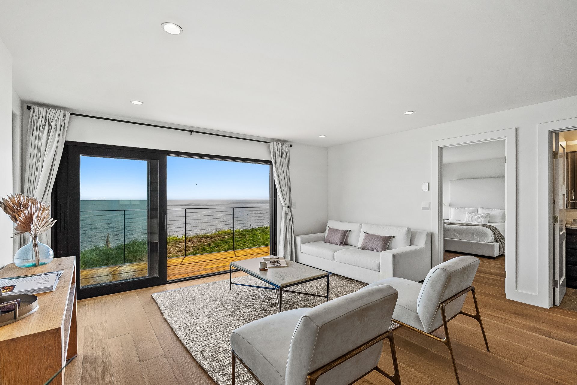 Bright living room with sofa, chairs, coffee table, and sliding glass doors opening to a sea view