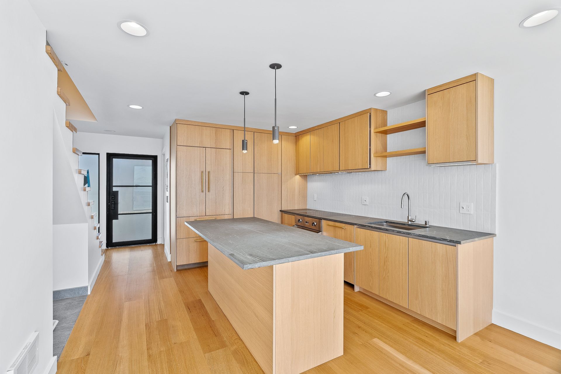 Modern kitchen with light wood cabinets, granite island, stainless sink, and hardwood floors.