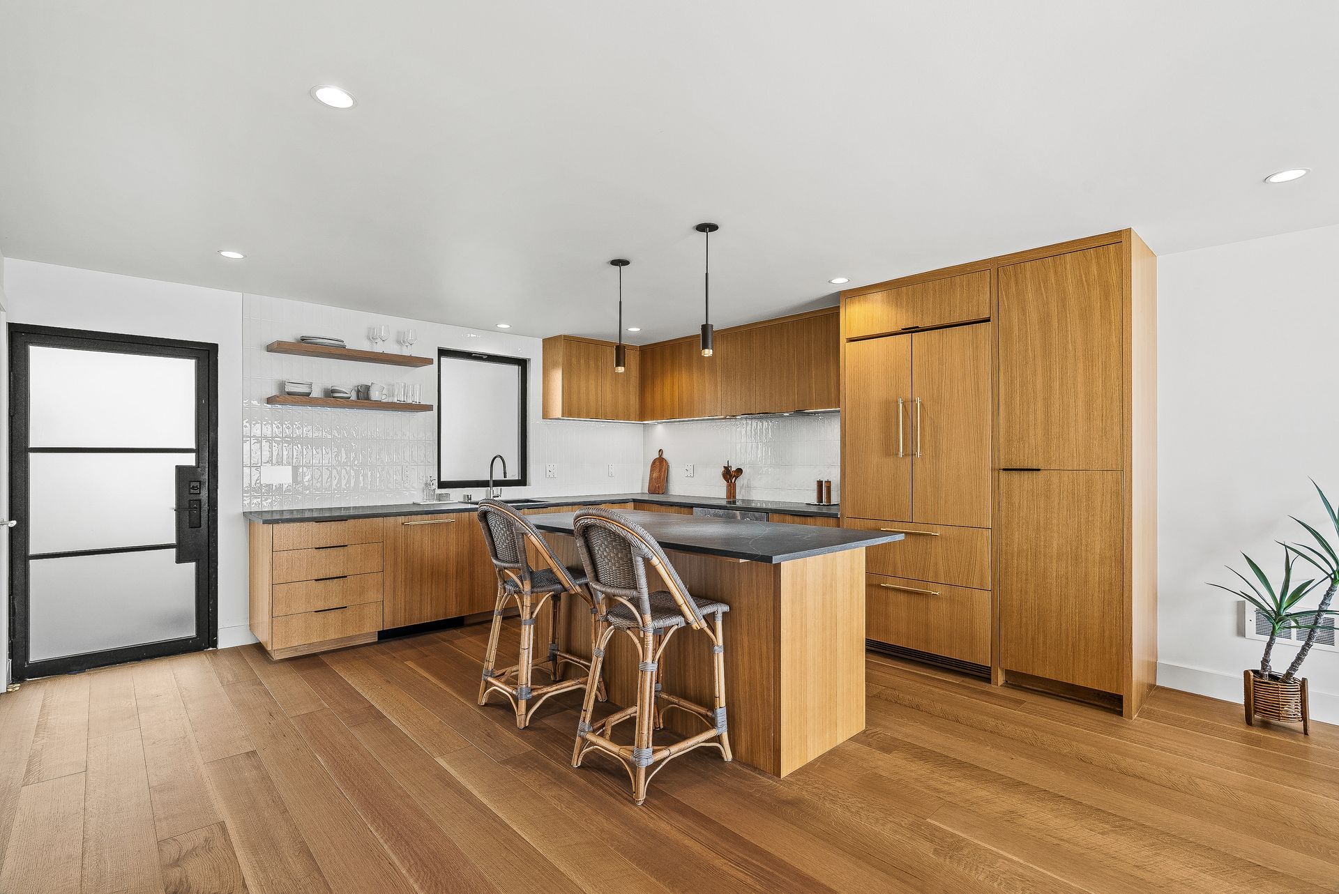 Modern kitchen with wood cabinets, island seating, black fixtures, and light wood flooring