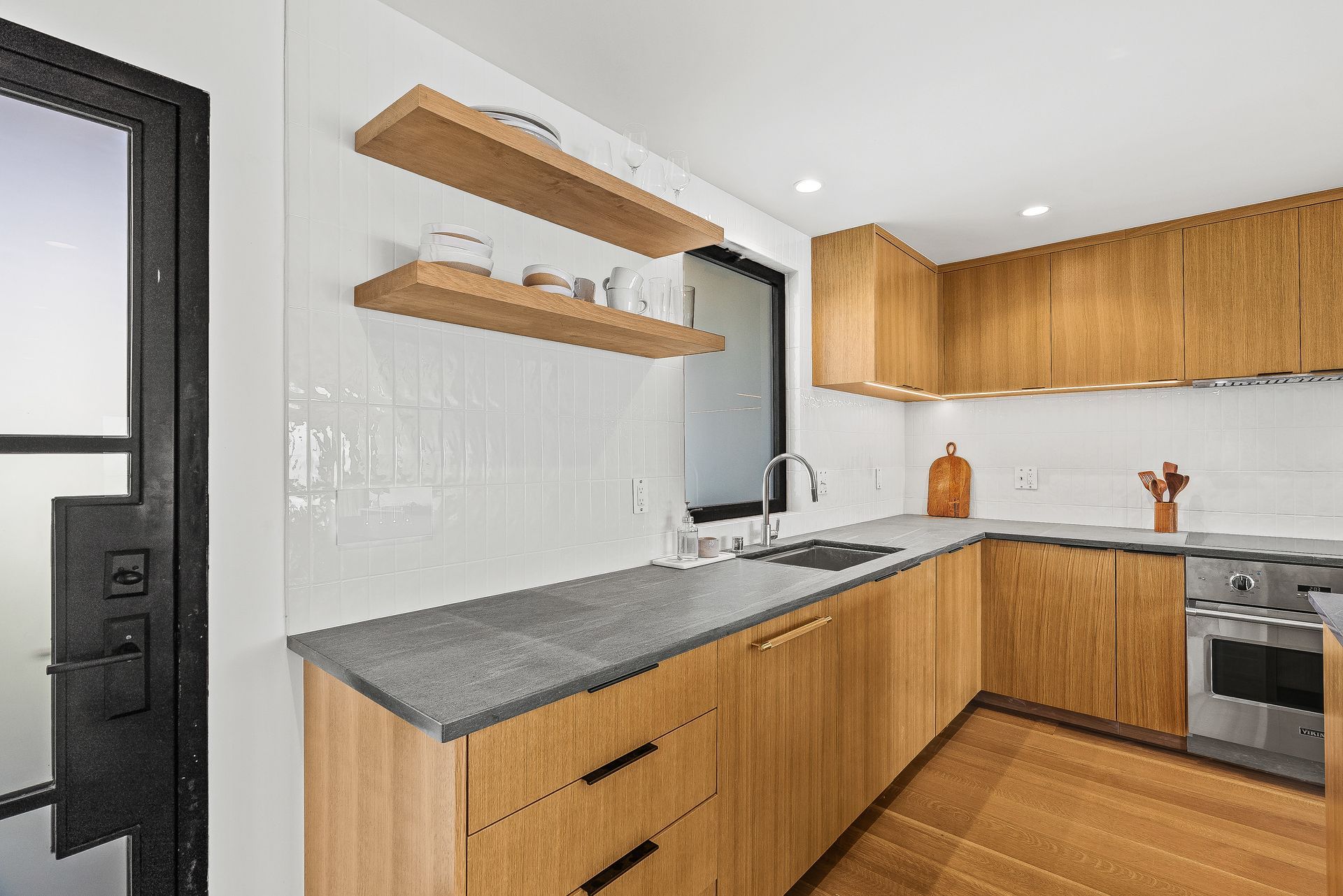 Modern kitchen with wood cabinets, gray countertops, open shelves, and white tile backsplash