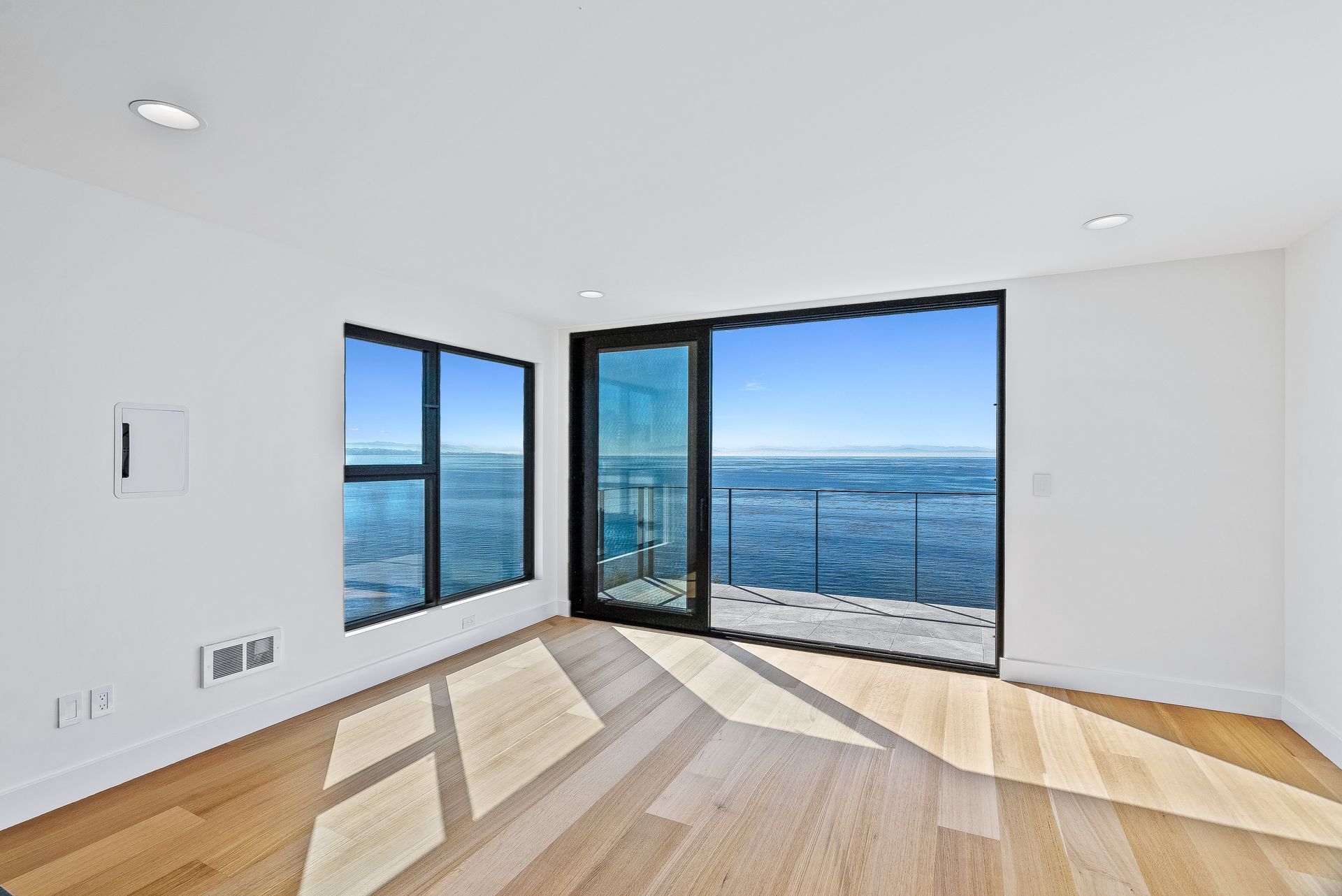 Bright empty room with wood floors, large windows, and ocean views