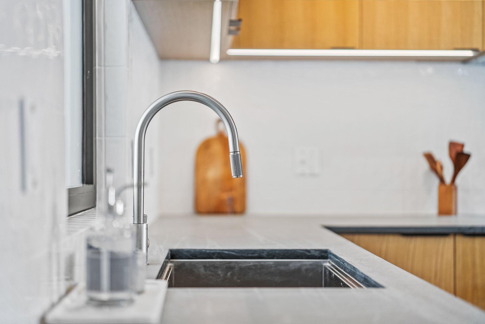 Modern kitchen sink with chrome faucet, white countertop, and wood cabinets in the background