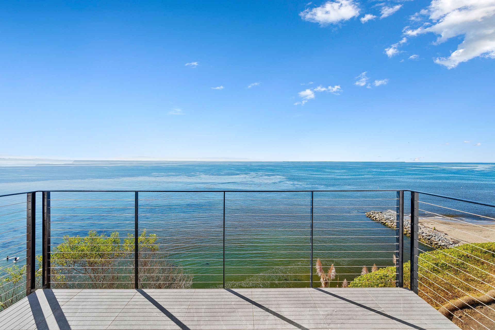Ocean view from a balcony with glass railing under a bright blue sky