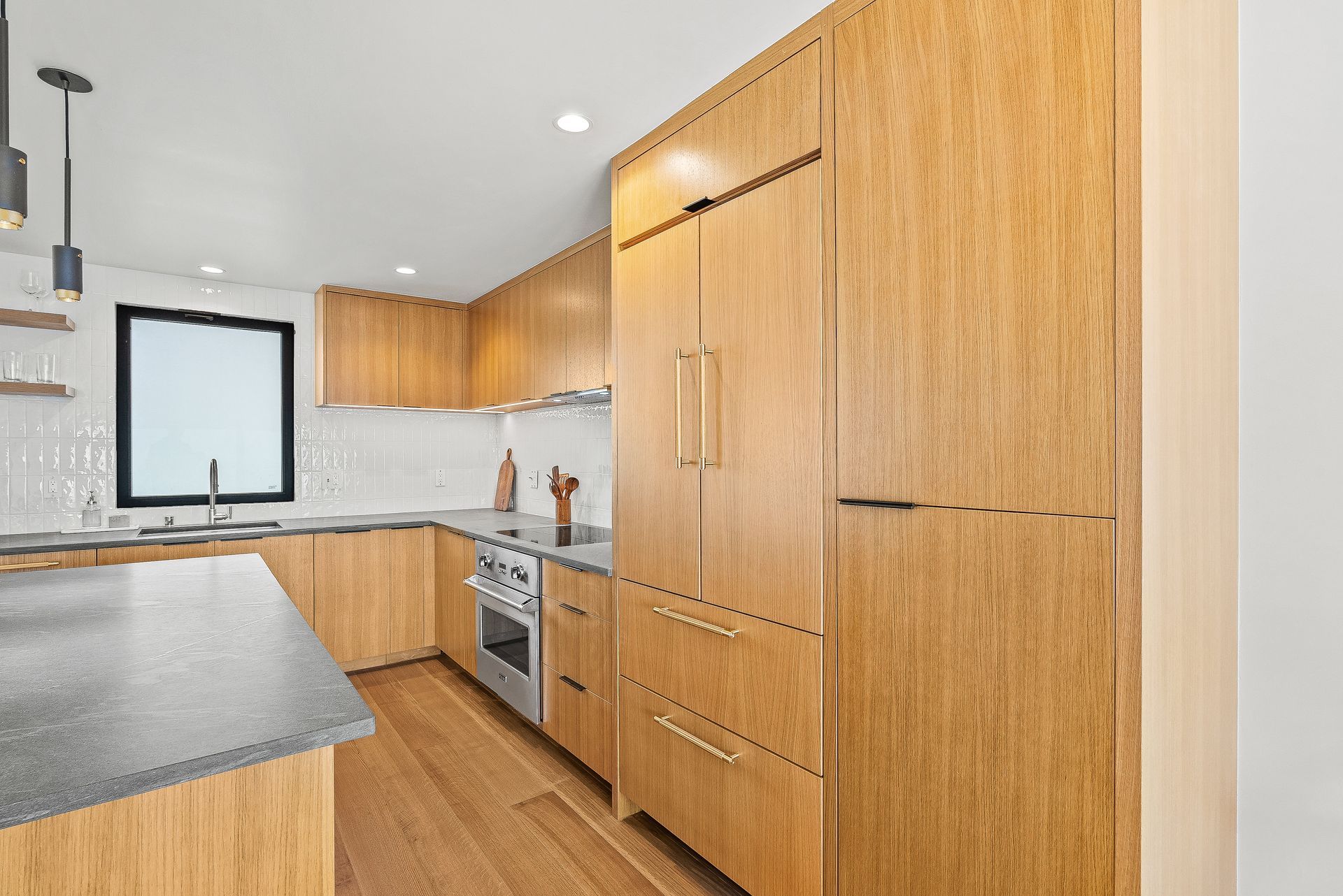 Modern kitchen with light wood cabinets, gray countertops, stainless steel appliances, and a window over the sink