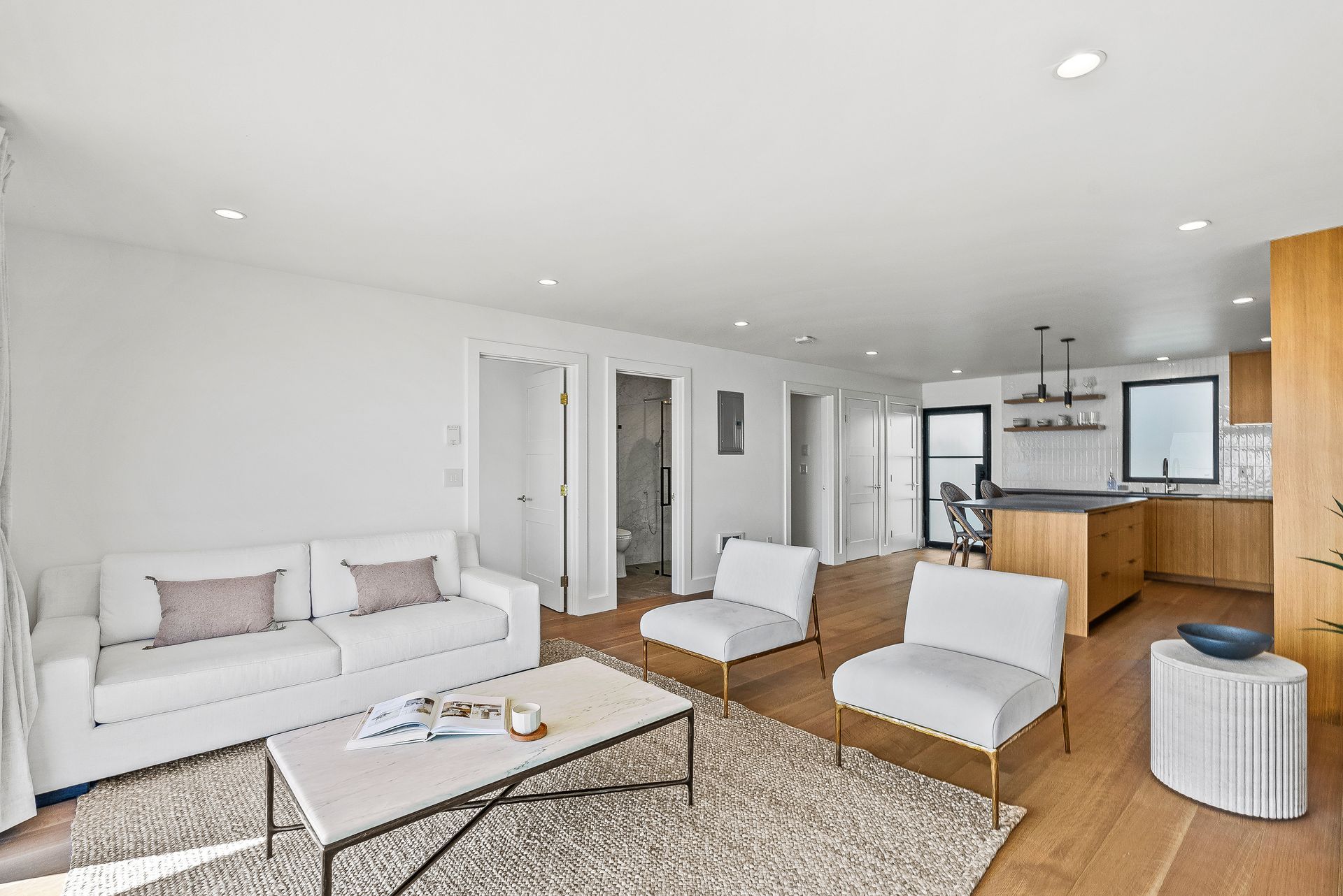 Modern living room with white sofa, chaise lounge, coffee table, and open kitchen with wood cabinets