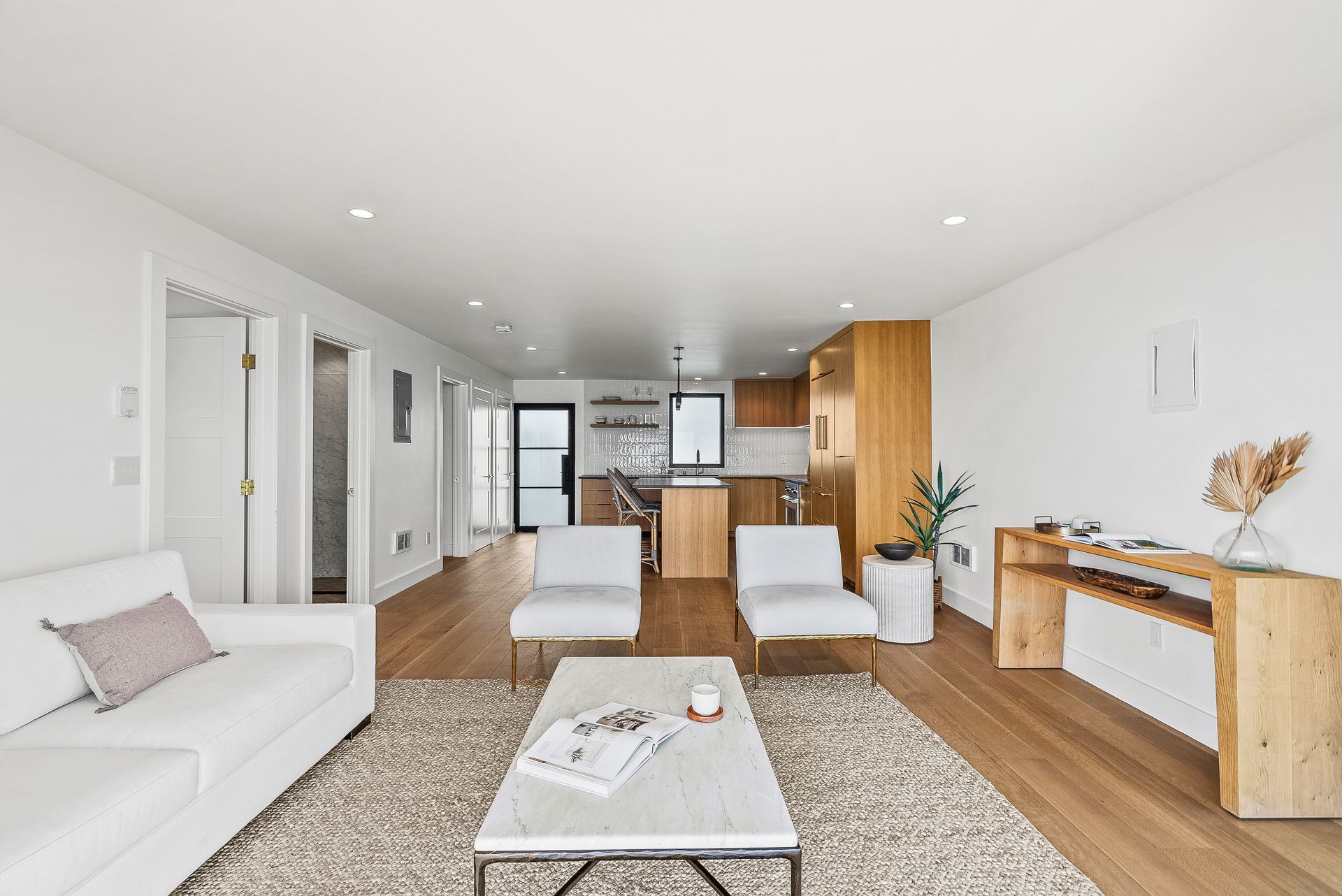 Bright modern living room with white sofa, coffee table, dining area, and kitchen in the background