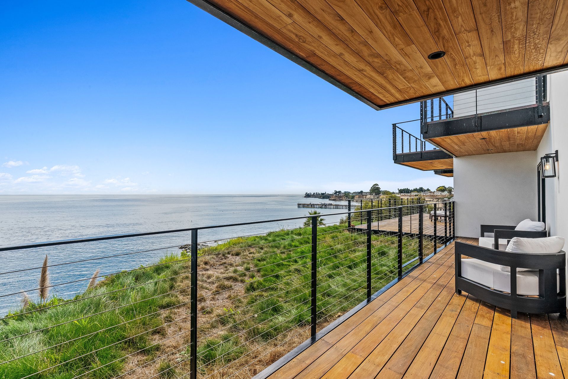 Oceanfront deck with black railing, wood flooring, and a seating area overlooking the water