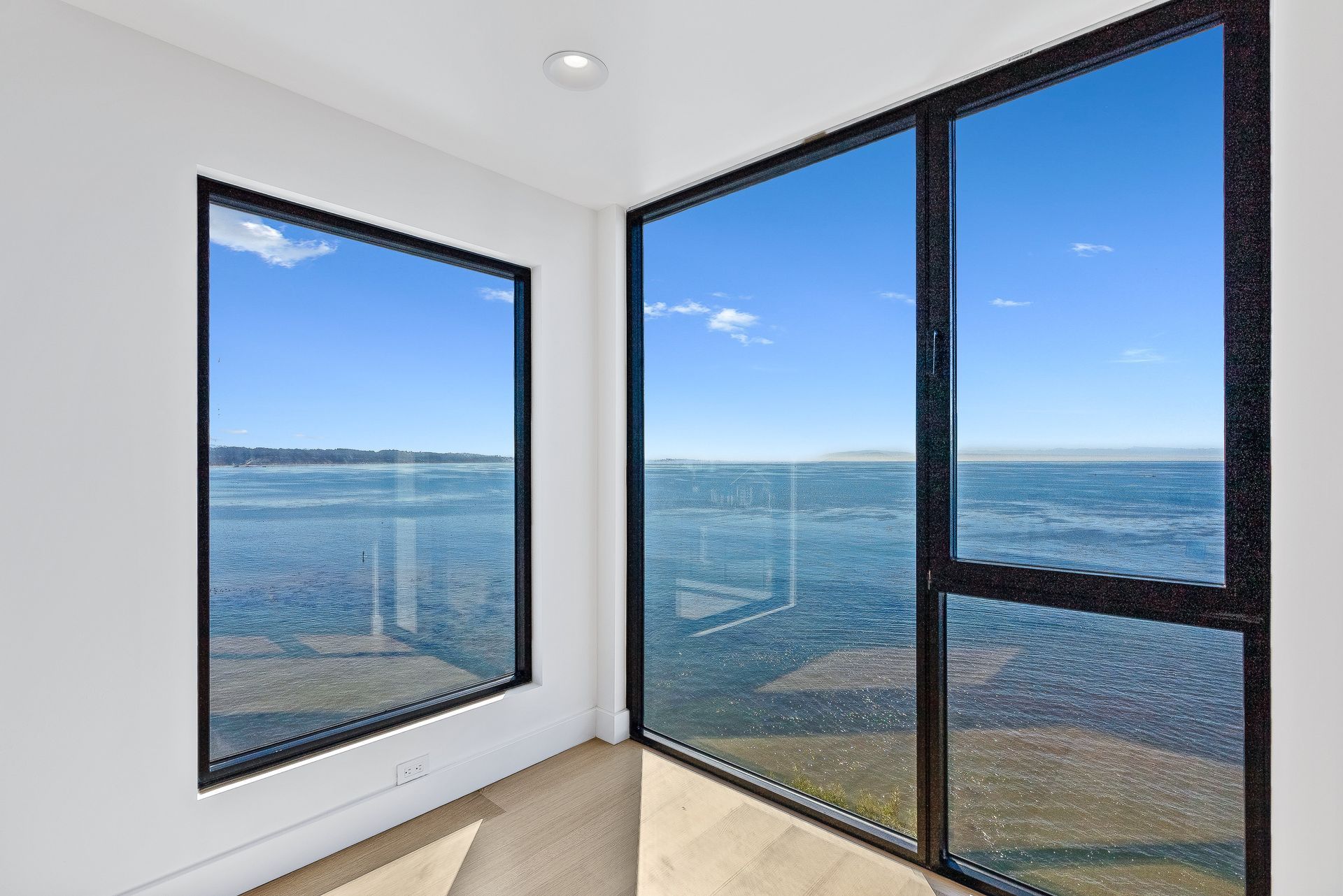 Bright corner room with large windows overlooking a calm blue ocean and sky.