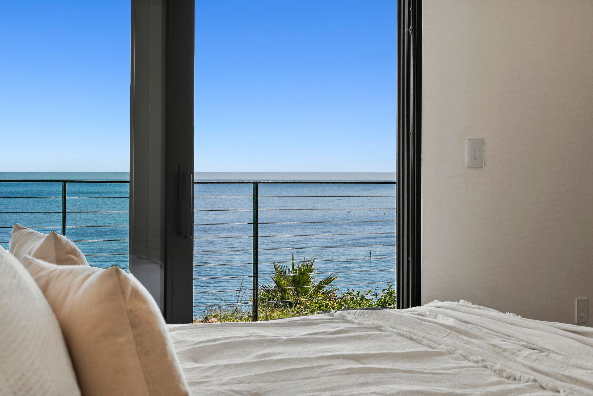 Bedroom with bed facing large windows and a calm ocean view at sunset