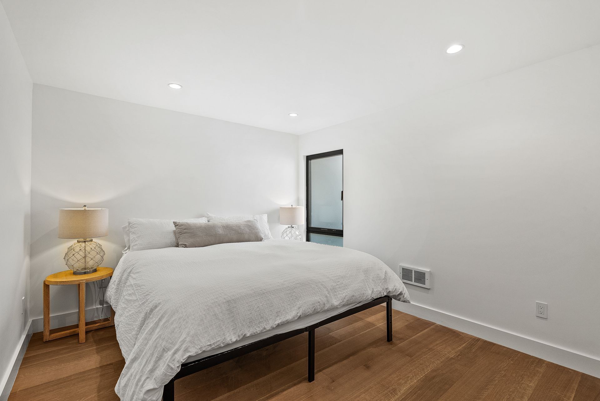 Minimal white bedroom with a bed, nightstand, lamp, and wood flooring