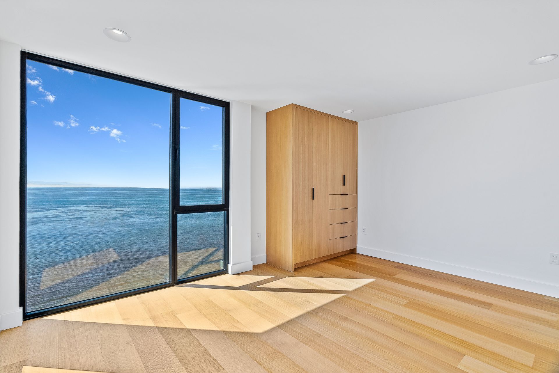 Bright room with wood floors, a closet, and large glass doors opening to an ocean view.