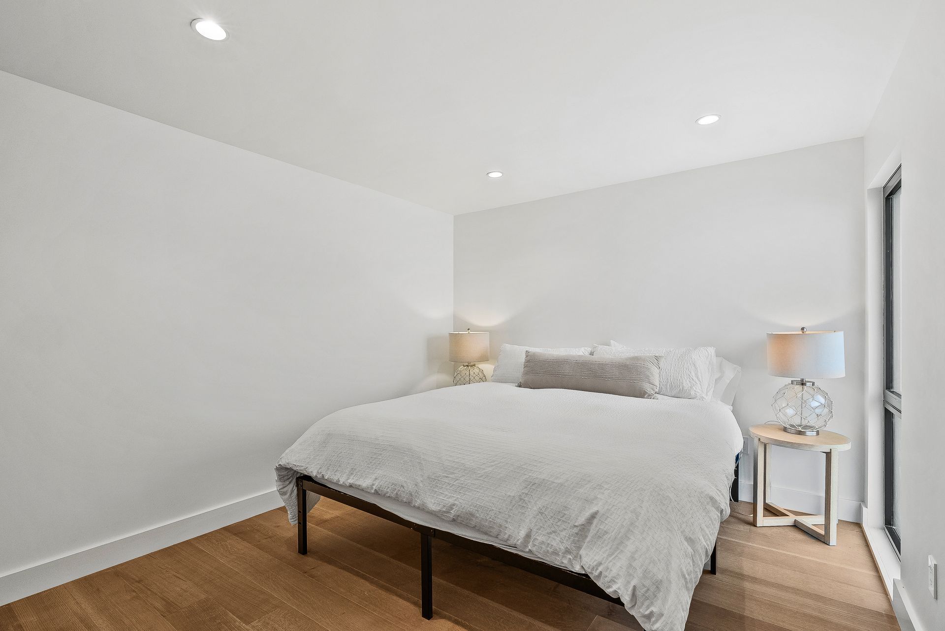 Bright minimalist bedroom with a queen bed, white walls, wood floor, and two bedside lamps