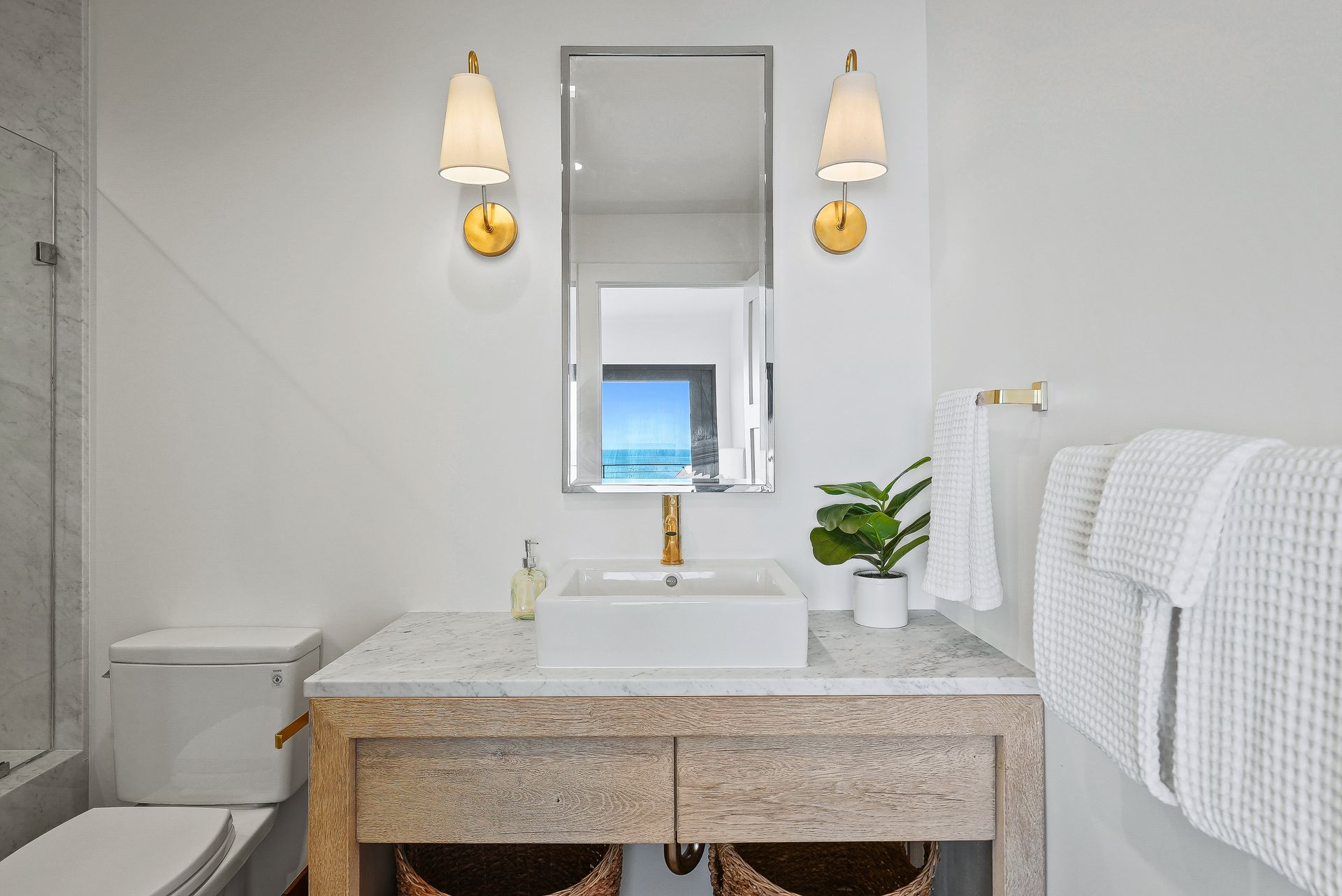 Bright bathroom vanity with granite counter, mirror, wall sconces, and white towels beside a shower.
