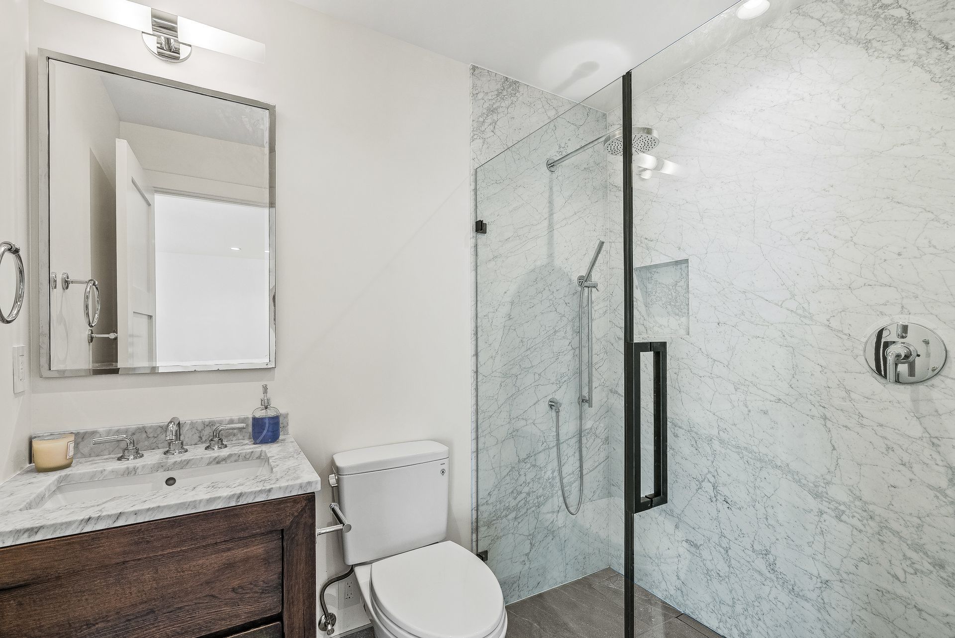 Bright bathroom with marble shower, vanity sink, mirror, and toilet