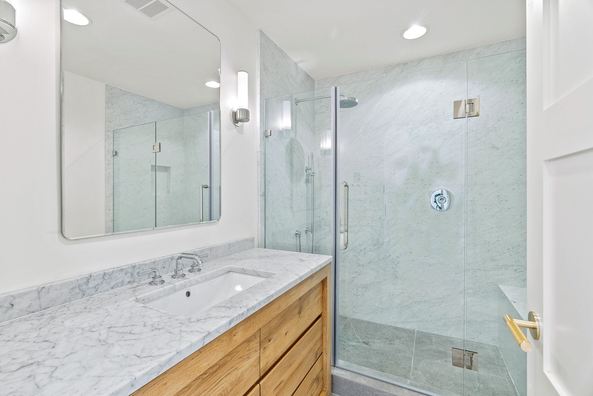 Bright modern bathroom with a white vanity, marble countertop, large mirror, and glass shower