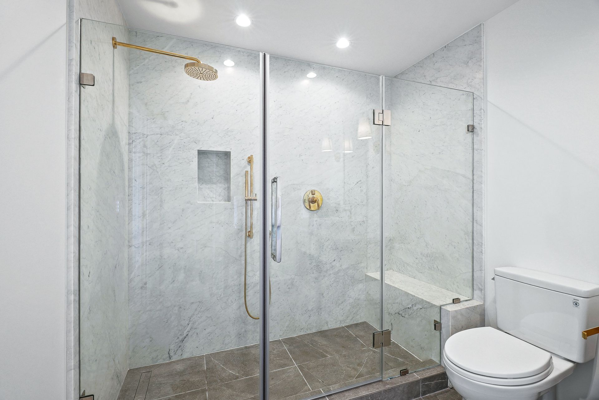 Modern bathroom with glass shower enclosure, rainfall showerhead, and toilet