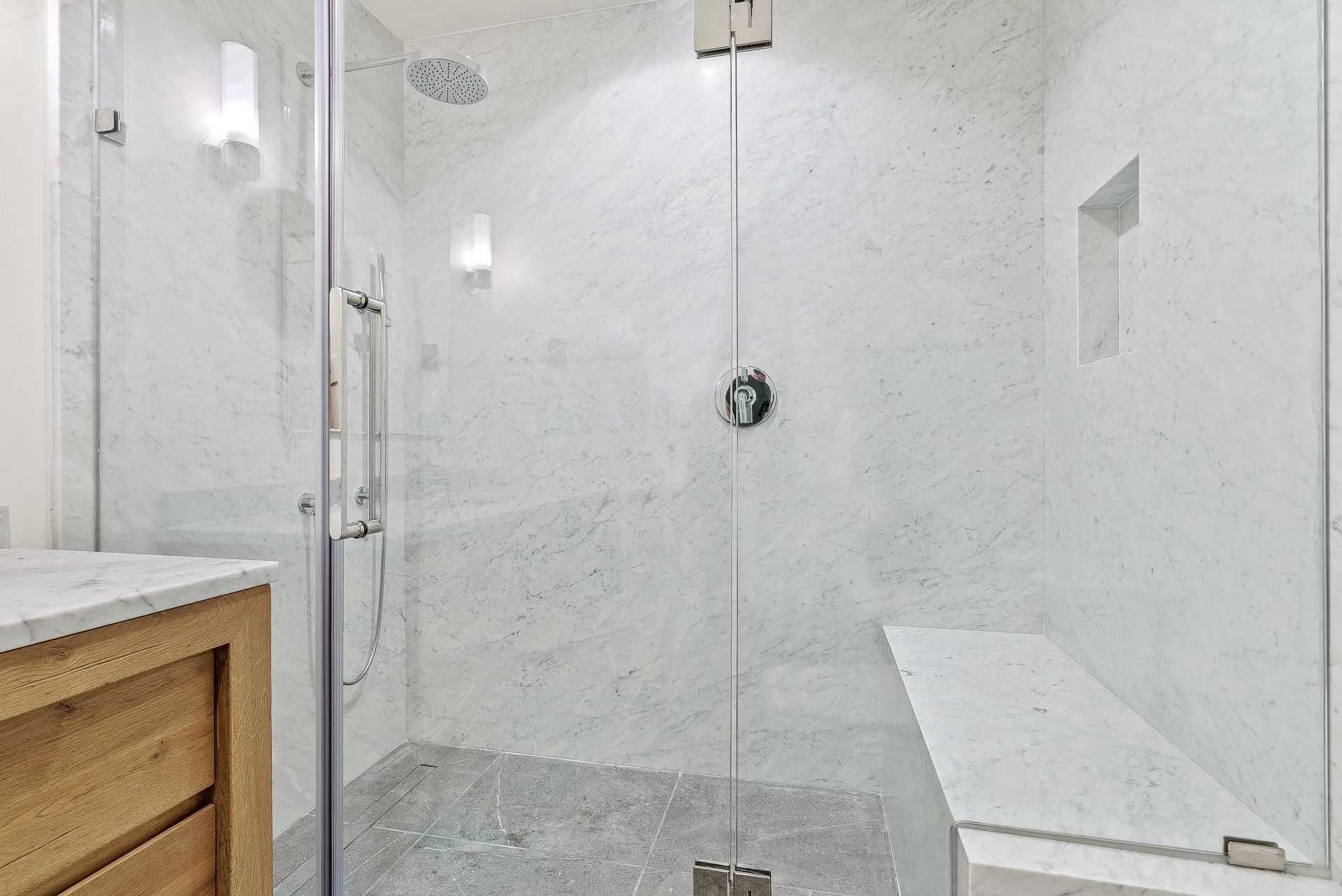 Modern bathroom with glass-enclosed shower, white tile walls, and wooden vanity edge
