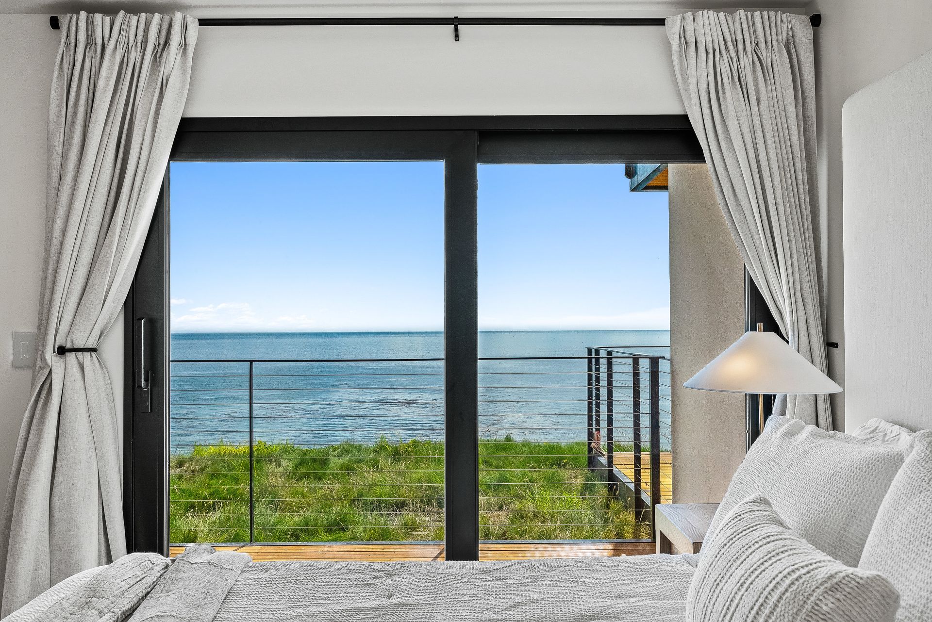 Bedroom with open curtains and a balcony view of the ocean and sky
