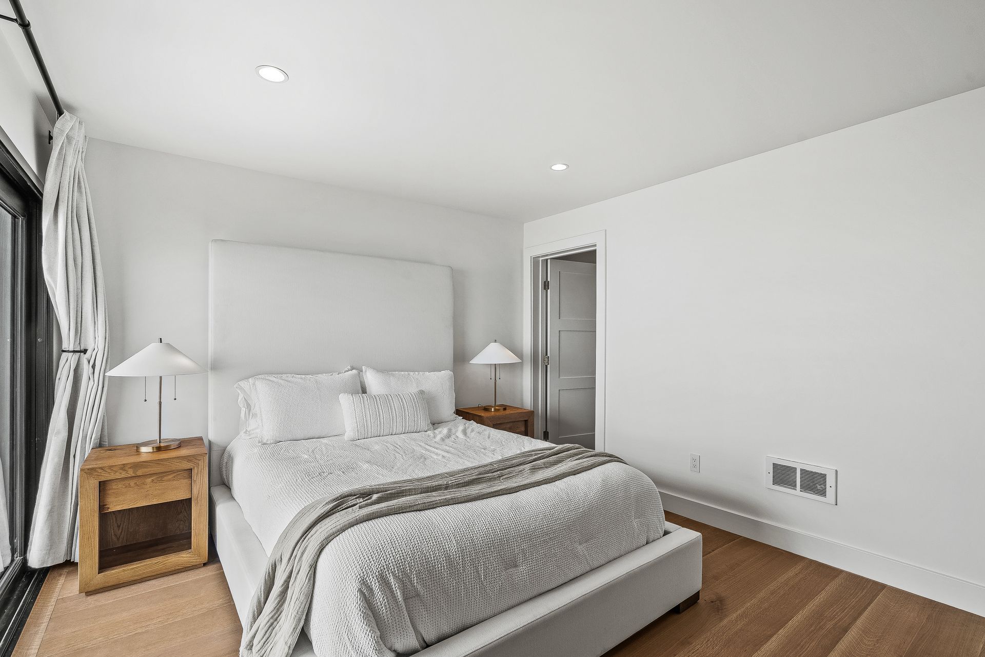 Bright modern bedroom with a white bed, wood nightstands, and large window curtains