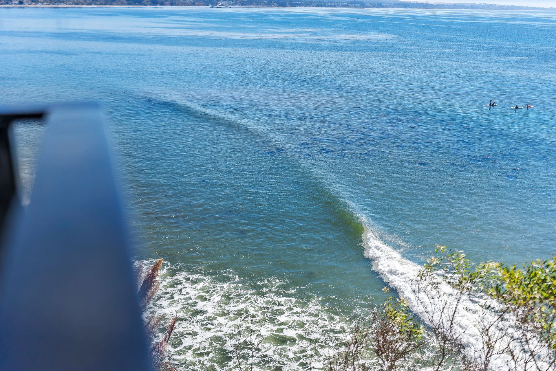 Ocean view from a rocky shore with a curling wave and blue water under bright sunlight