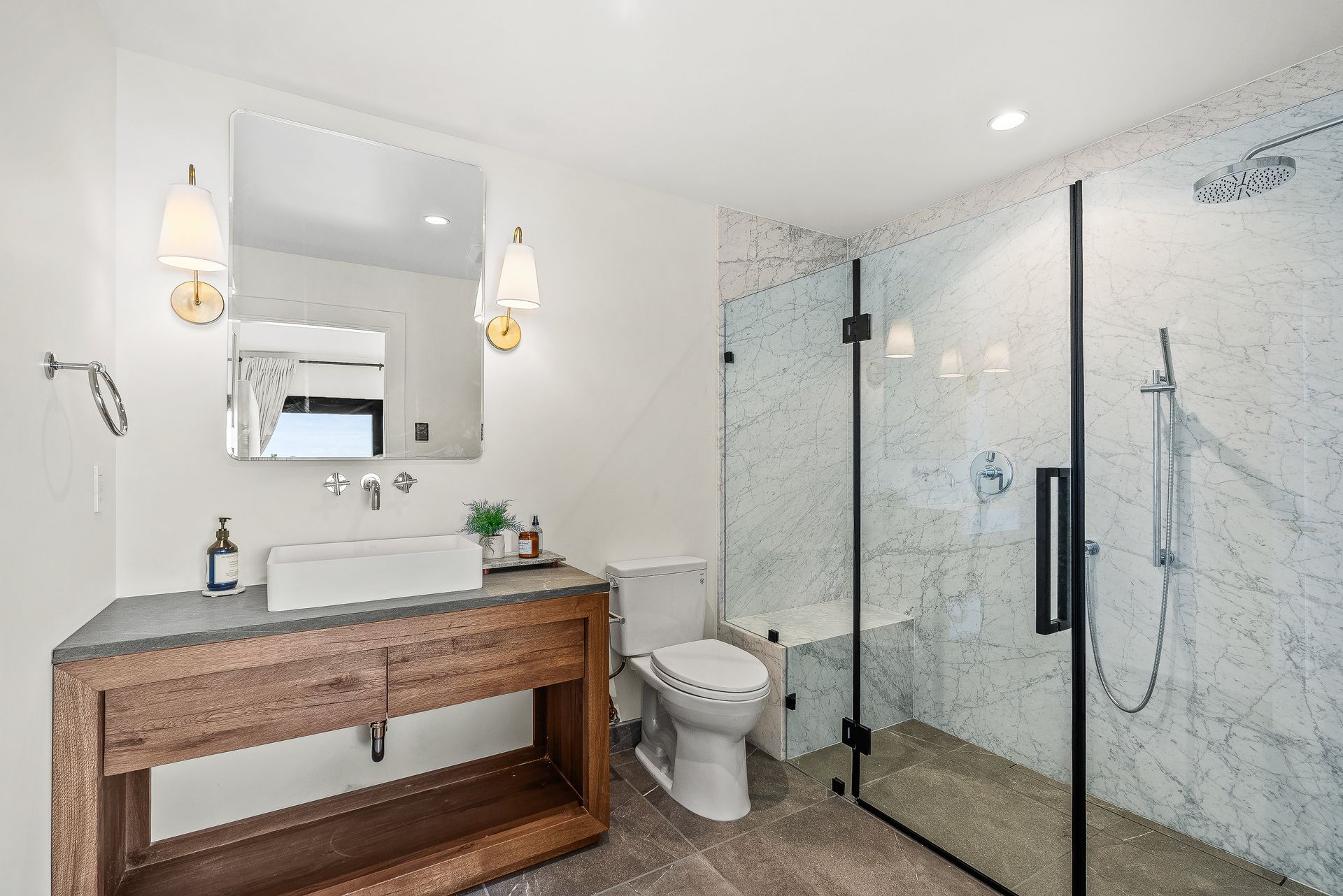 Modern bathroom with wood vanity, mirror, toilet, and glass walk-in shower in white tile.