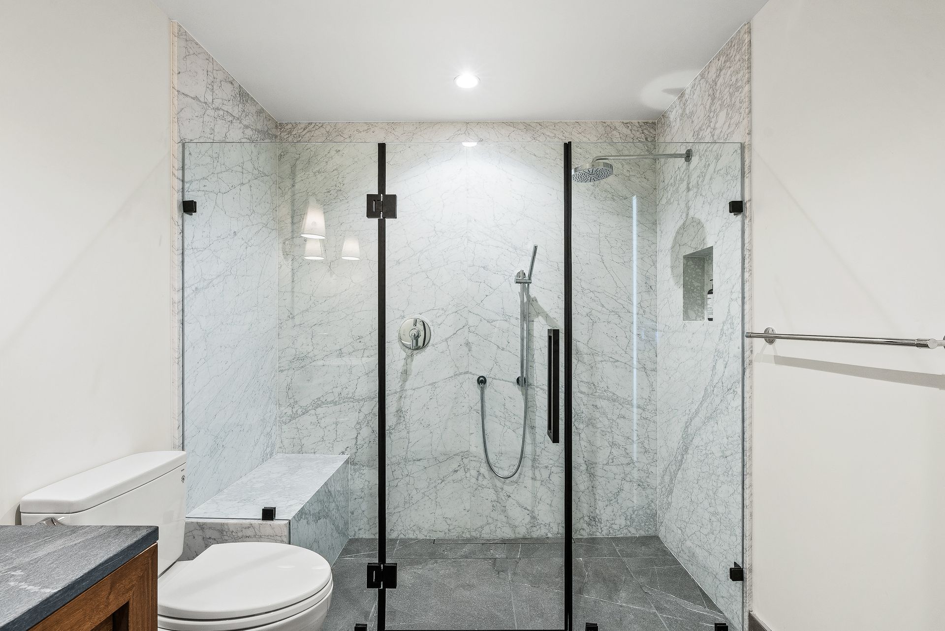 Modern bathroom with glass shower enclosure, toilet, and white marble-tiled walls